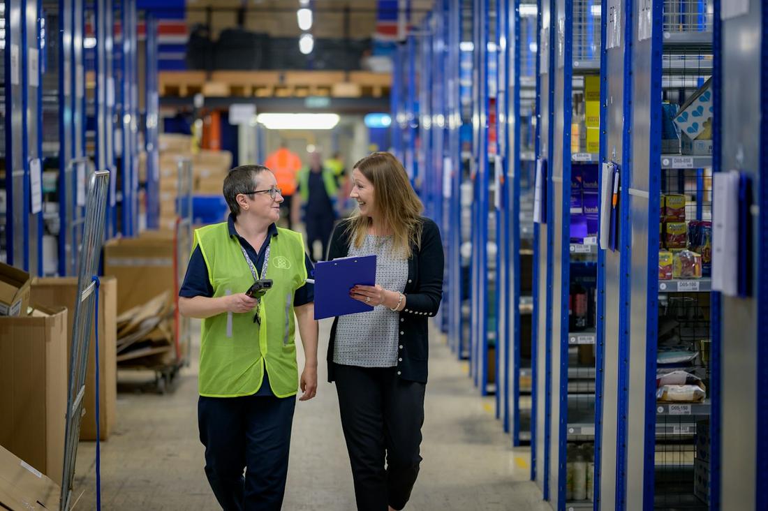 Two women talking as they walk through a warehouse aisle